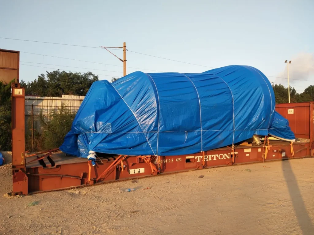 Thiết bị công nghiệp được bọc bạt chống thấm, gia cố bằng dây tăng đơ và cố định chắc chắn trước khi bốc lên mooc vận chuyển an toàn. thiet-bi-cong-nghiep-boc-bat-gia-co-truoc-khi-boc-len-mooc-van-chuyen