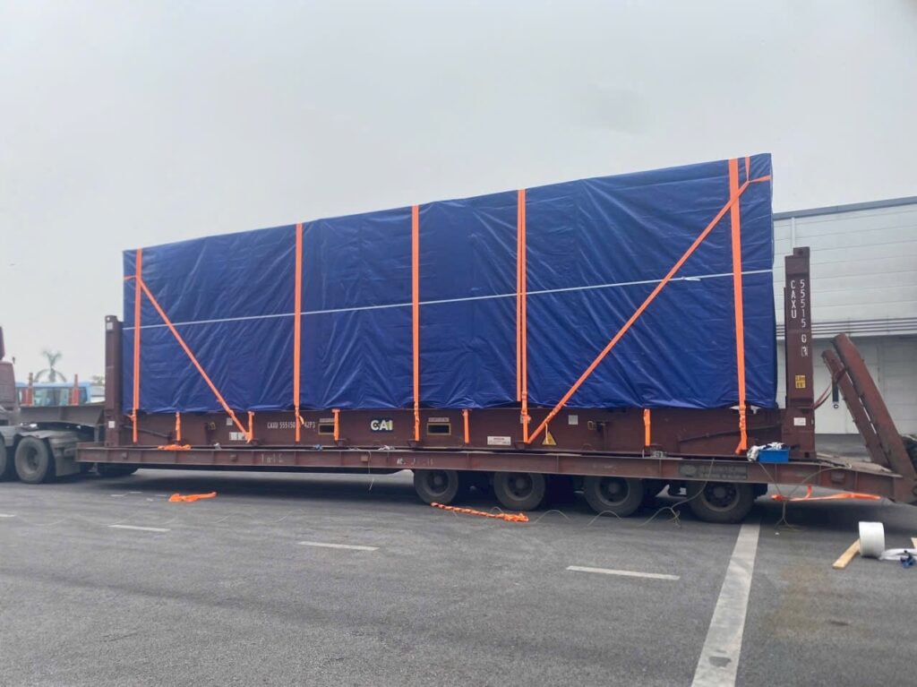 Hàng hóa được chằng buộc bằng dây tăng đơ, phủ bạt bảo vệ và cố định chắc chắn trên mooc lùn trước khi vận chuyển, bảo đảm an toàn trong suốt hành trình. chang-buoc-co-dinh-hang-hoa-tren-mooc-lun-truoc-khi-van-chuyen-an-toan-dung-chuan